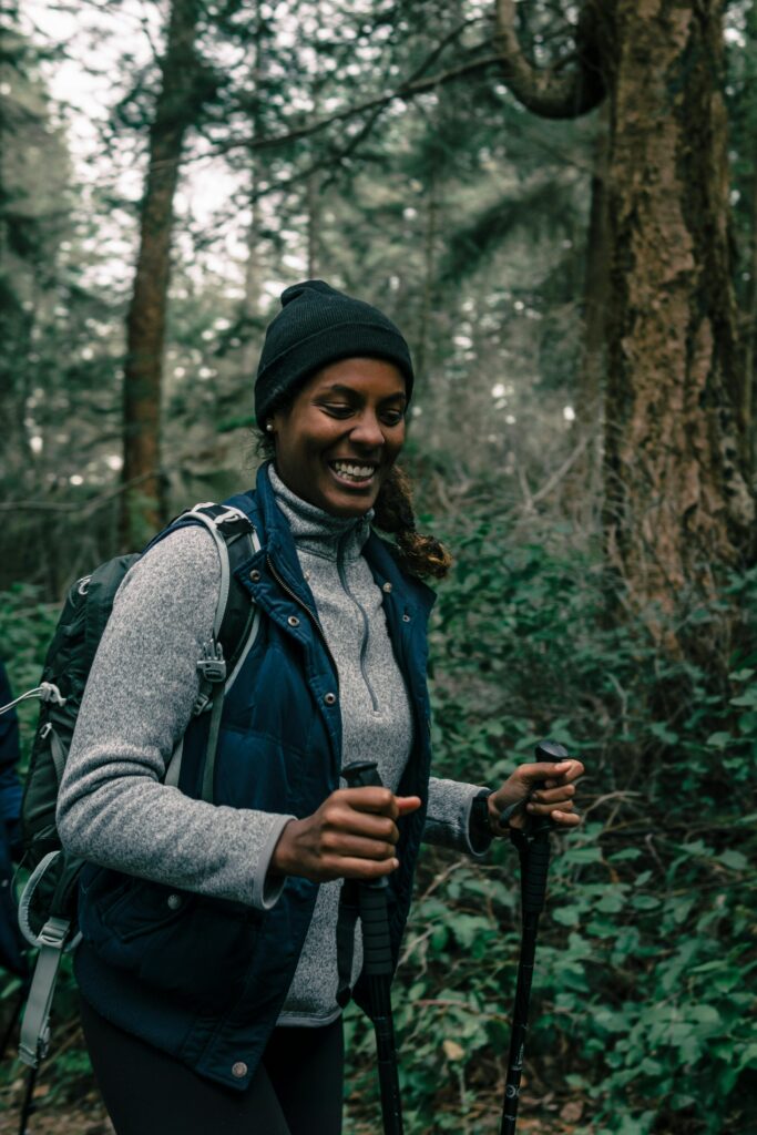 Black woman smiling while hiking with trekking poles in a forest.